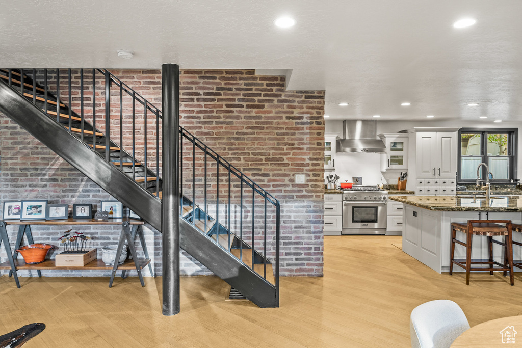 Kitchen featuring high end range, wall chimney exhaust hood, light wood finished floors, a kitchen breakfast bar, and recessed lighting