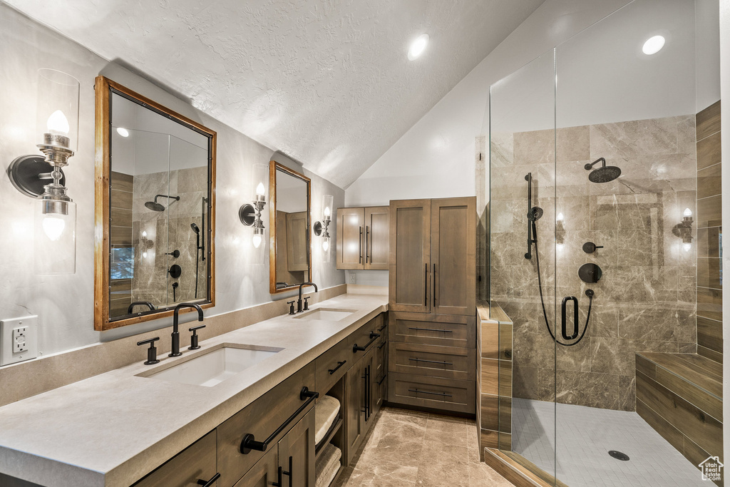 Full bathroom with lofted ceiling, a shower stall, a textured ceiling, and double vanity
