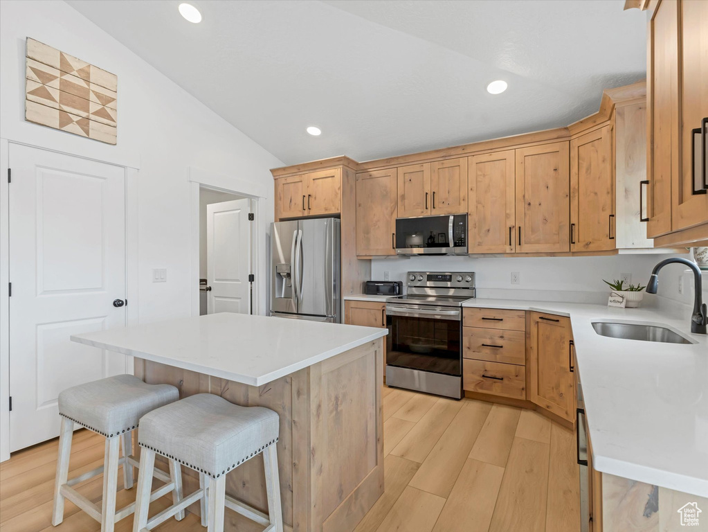 Kitchen featuring appliances with stainless steel finishes, a sink, lofted ceiling, light wood-type flooring, and a breakfast bar area