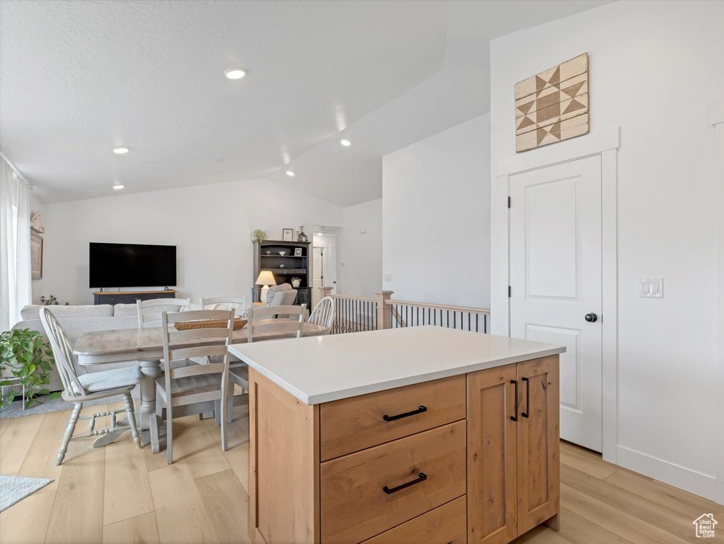 Kitchen featuring light wood finished floors, vaulted ceiling, a center island, recessed lighting, and light countertops