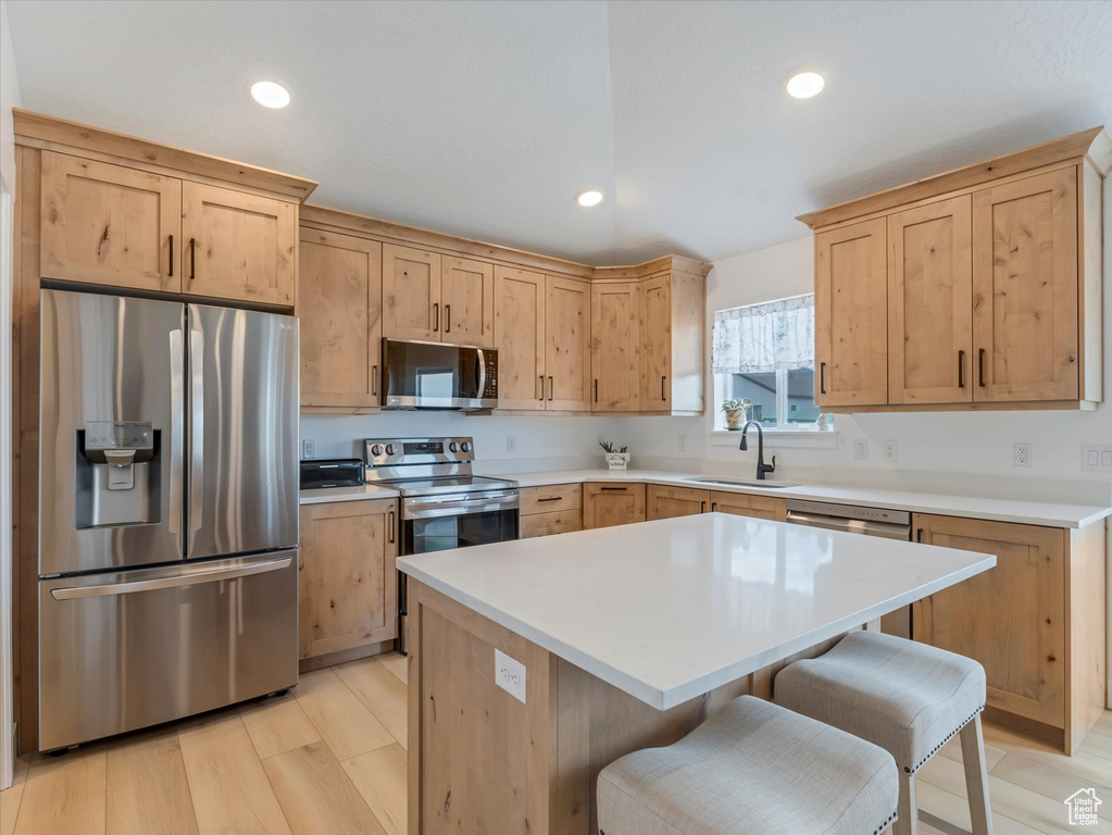 Kitchen with stainless steel appliances, a sink, light brown cabinets, a breakfast bar, and recessed lighting