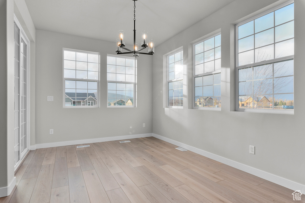 Unfurnished dining area with a chandelier, light wood-style floors, and baseboards