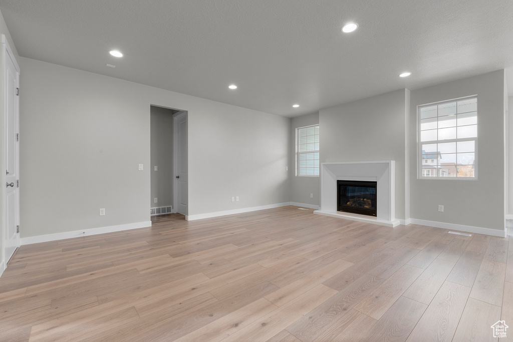 Unfurnished living room with a glass covered fireplace, light wood-type flooring, recessed lighting, and baseboards