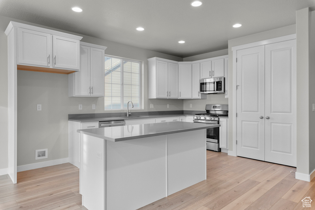 Kitchen with appliances with stainless steel finishes, light wood finished floors, white cabinets, baseboards, and recessed lighting