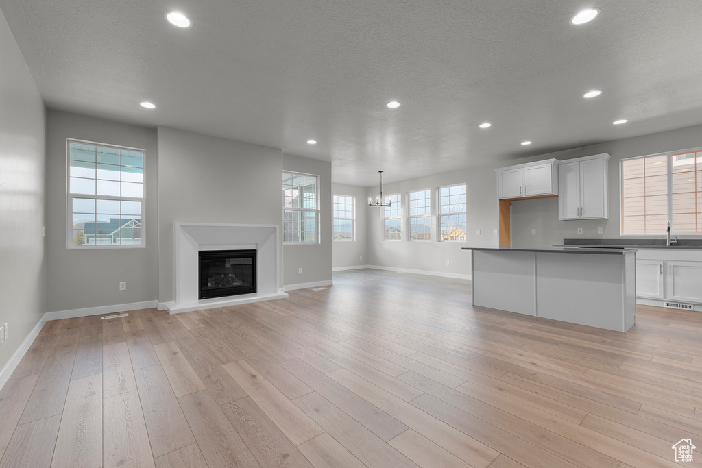 Unfurnished living room featuring recessed lighting, a chandelier, baseboards, a glass covered fireplace, and light wood-type flooring