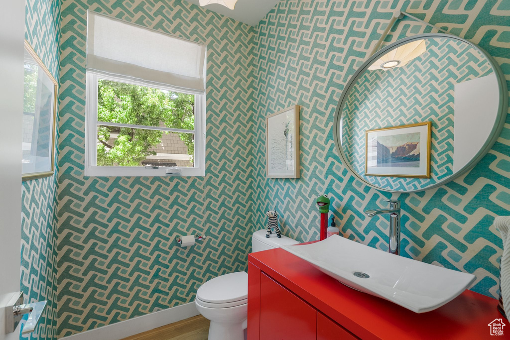 Half bath with wallpapered walls, toilet, a sink, and wood finished floors