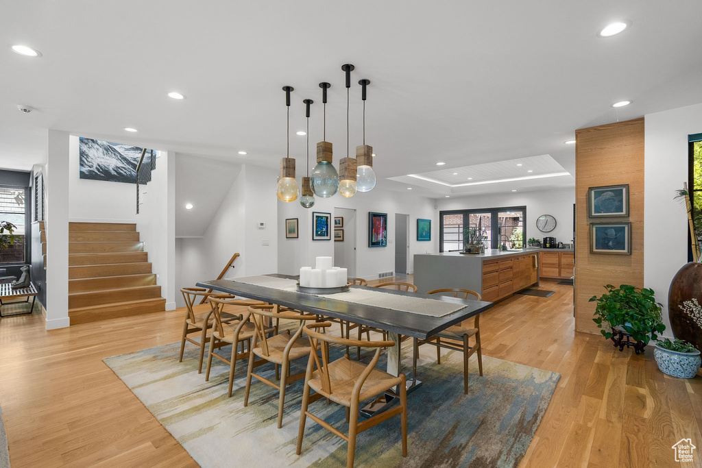 Dining space featuring light wood-type flooring, recessed lighting, stairs, plenty of natural light, and a raised ceiling