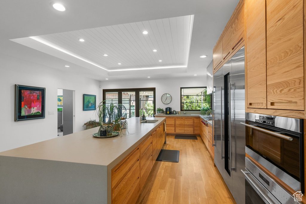 Kitchen featuring modern cabinets, a sink, a tray ceiling, light wood-style floors, and recessed lighting
