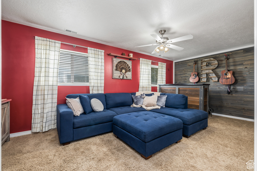 Carpeted living room with a ceiling fan, a textured ceiling, baseboards, and wooden walls