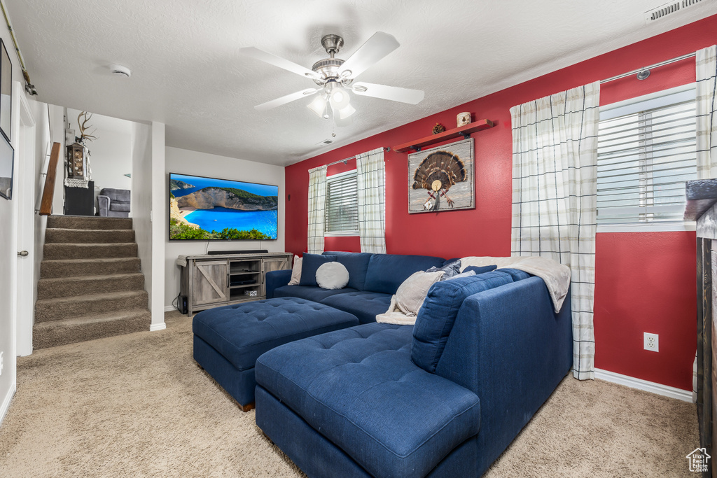 Carpeted living area with stairs, ceiling fan, and baseboards
