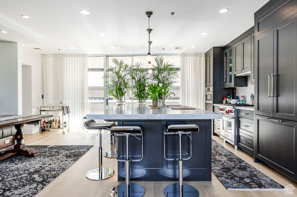 Kitchen featuring a sink, stainless steel appliances, light wood-style flooring, a kitchen breakfast bar, and light stone counters