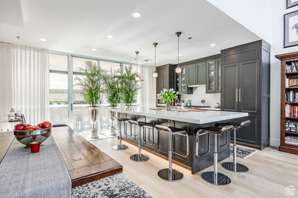 Kitchen with light wood-type flooring, a kitchen breakfast bar, glass insert cabinets, a center island with sink, and decorative light fixtures
