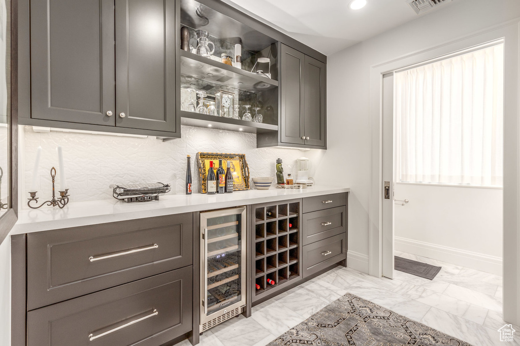 Indoor dry bar featuring beverage cooler, light marble finish floors, baseboards, tasteful backsplash, and recessed lighting