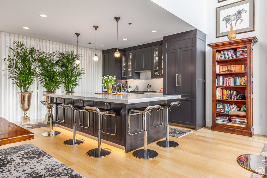 Indoor bar with light wood finished floors, hanging light fixtures, recessed lighting, and decorative backsplash