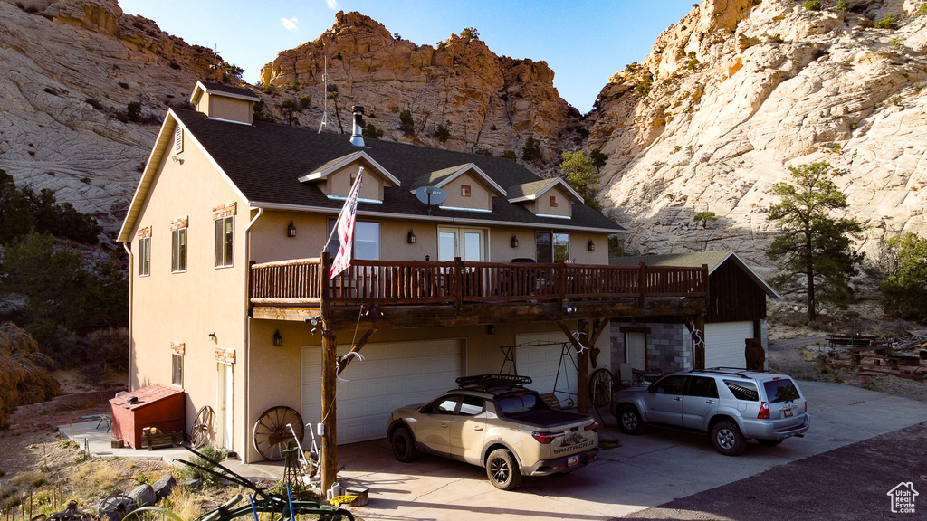 View of front of house featuring driveway, a deck with mountain view, stucco siding, an attached garage, and roof with shingles