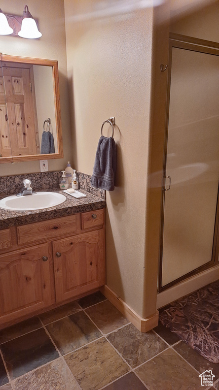 Full bath with a shower stall, baseboards, vanity, and stone finish floors