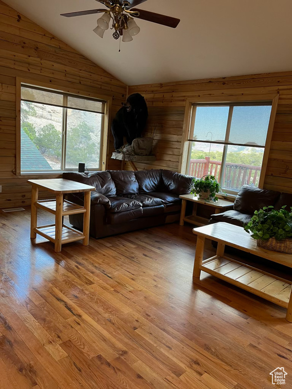Living area featuring wood walls, lofted ceiling, plenty of natural light, light wood finished floors, and ceiling fan