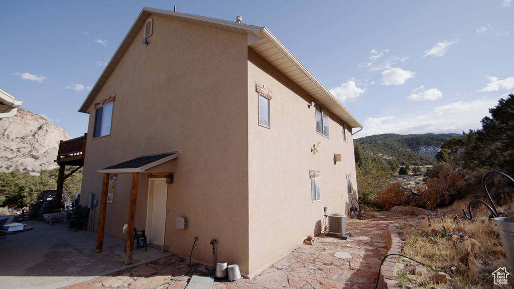 View of side of property with a mountain view, stucco siding, central AC unit, a balcony, and a patio area
