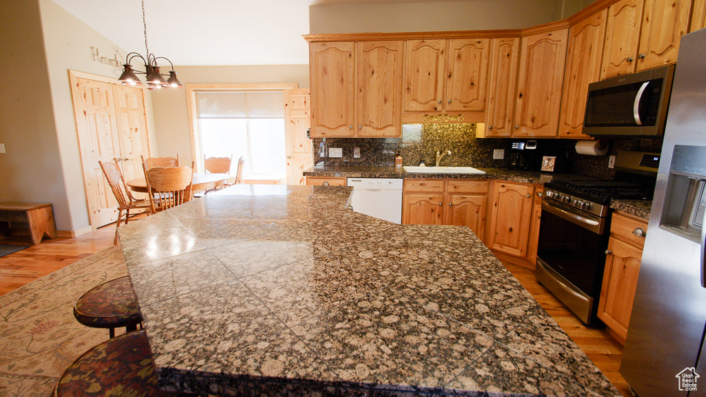 Kitchen with stainless steel appliances, a sink, light wood finished floors, decorative backsplash, and a chandelier