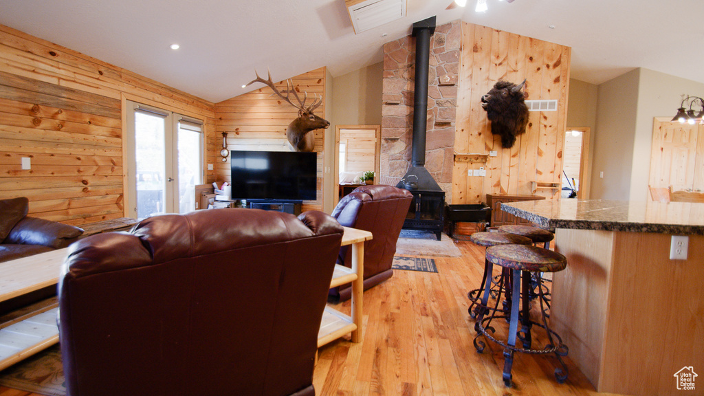 Living room featuring a wood stove, lofted ceiling, wooden walls, and light wood-style flooring