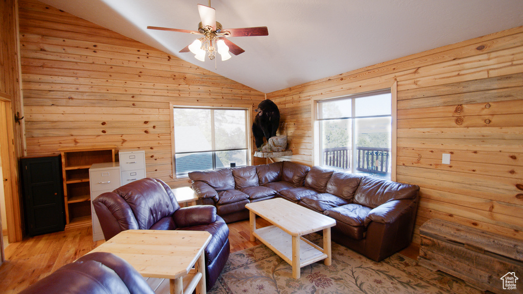Living area featuring vaulted ceiling, wooden walls, ceiling fan, and wood finished floors