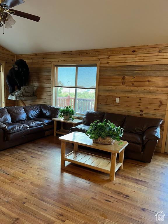 Living room with a ceiling fan, wooden walls, vaulted ceiling, and light wood-style flooring