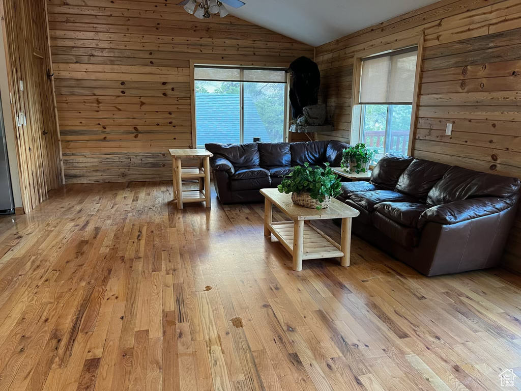 Living area with wooden walls, plenty of natural light, lofted ceiling, light wood finished floors, and a ceiling fan