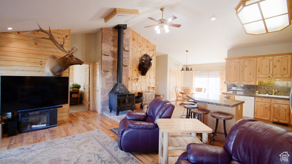 Living room with a wood stove, a ceiling fan, light wood-style flooring, and high vaulted ceiling