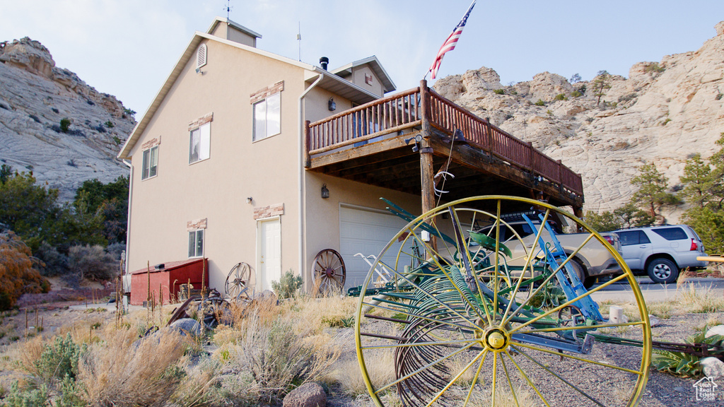 View of side of home featuring stucco siding, a deck with mountain view, and an attached garage