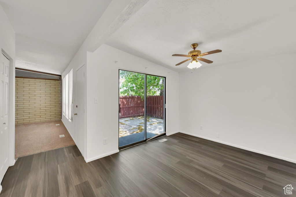 Empty room featuring dark wood-style floors, vaulted ceiling, a ceiling fan, baseboards, and brick wall