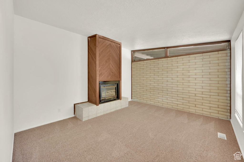 Unfurnished living room with a tile fireplace, carpet floors, and brick wall