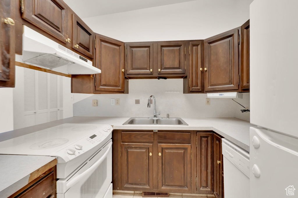 Kitchen with white appliances, a sink, under cabinet range hood, and light countertops