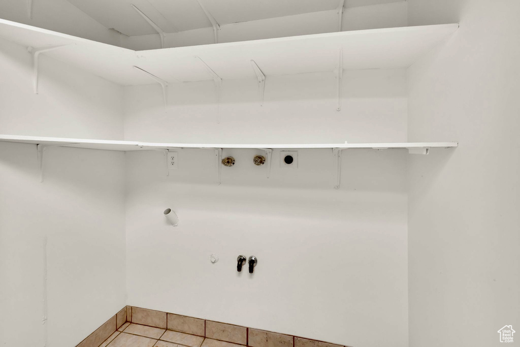 Laundry area with electric dryer hookup, gas dryer hookup, hookup for a washing machine, light tile patterned floors, and baseboards
