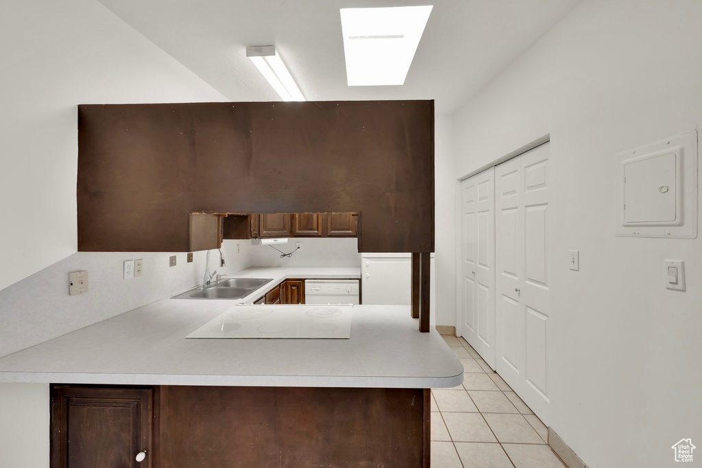 Kitchen featuring a sink, light countertops, light tile patterned flooring, a peninsula, and white electric cooktop