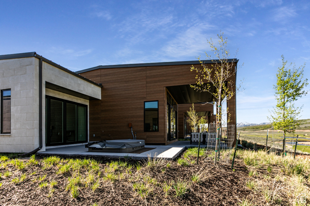 Back of property featuring a covered hot tub, a patio, and fence