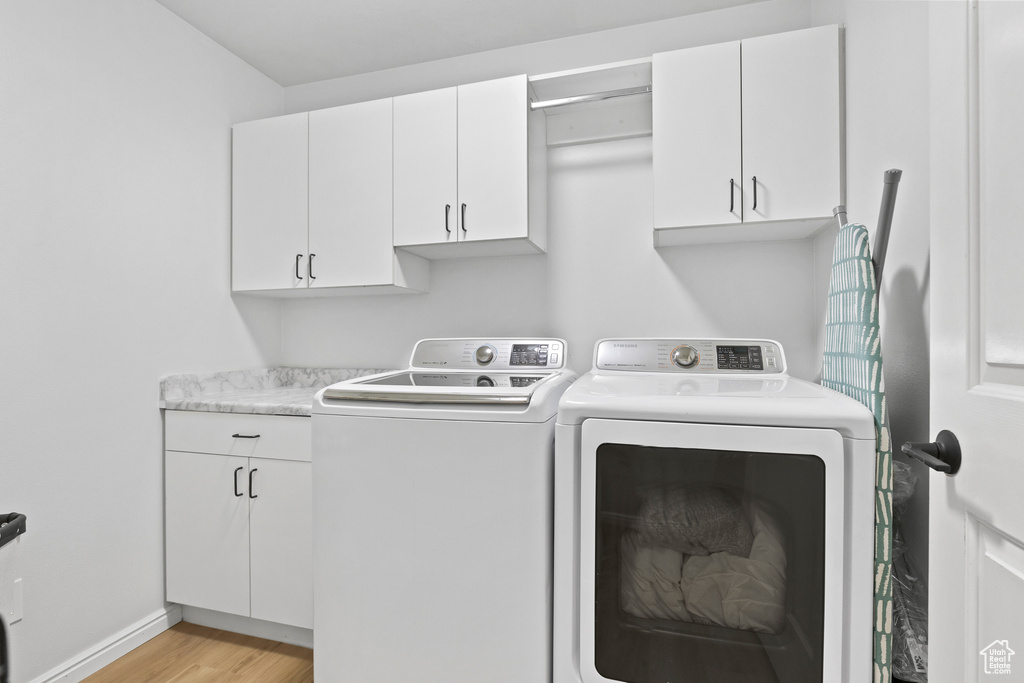 Laundry area with washer and clothes dryer, cabinet space, light wood-style flooring, and baseboards