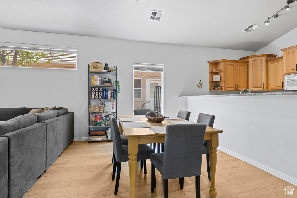 Dining area featuring light wood-style flooring, lofted ceiling, rail lighting, and baseboards