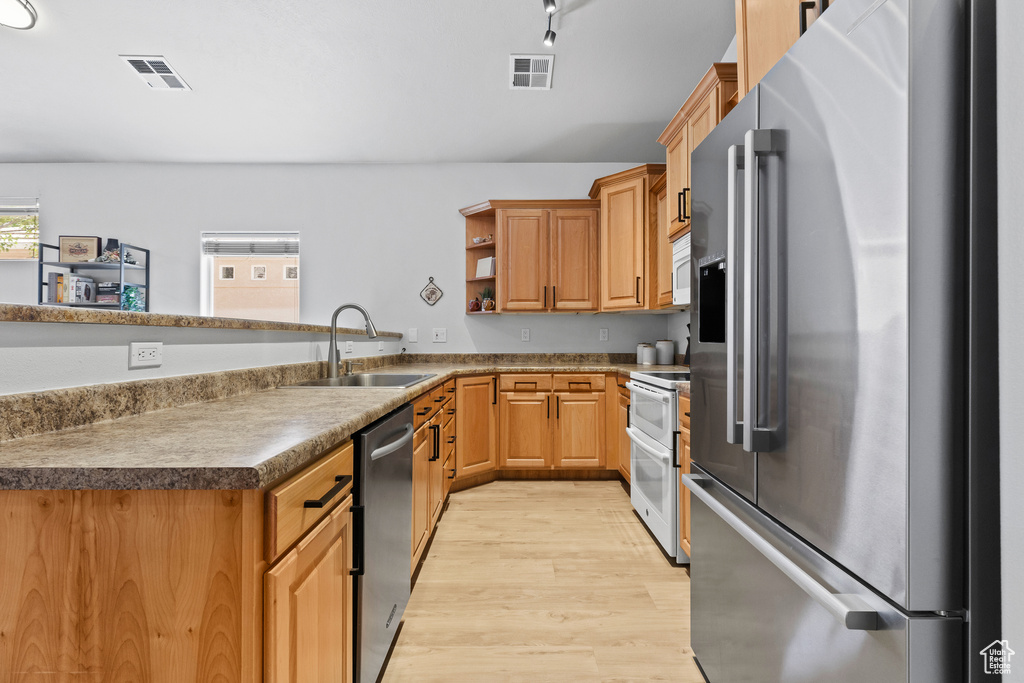 Kitchen with appliances with stainless steel finishes, a sink, light wood-style floors, open shelves, and a peninsula
