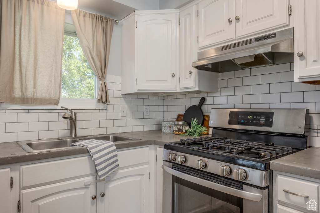 Kitchen featuring stainless steel gas stove, under cabinet range hood, a sink, white cabinetry, and backsplash
