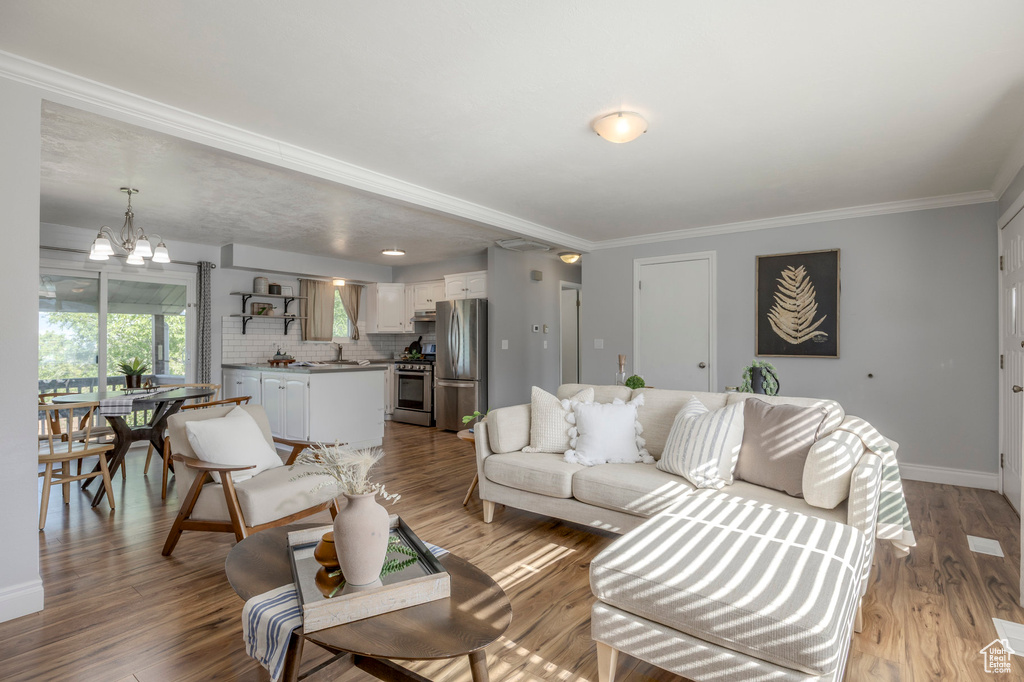 Living room with a chandelier, crown molding, baseboards, and light wood-type flooring