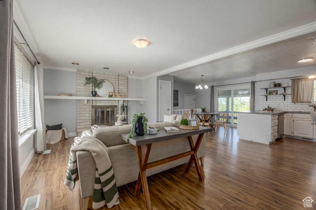 Living area with a chandelier, crown molding, dark wood-style floors, baseboards, and a brick fireplace