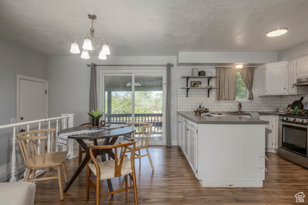 Kitchen featuring stainless steel range with gas stovetop, decorative backsplash, white cabinetry, dark wood-type flooring, and a chandelier