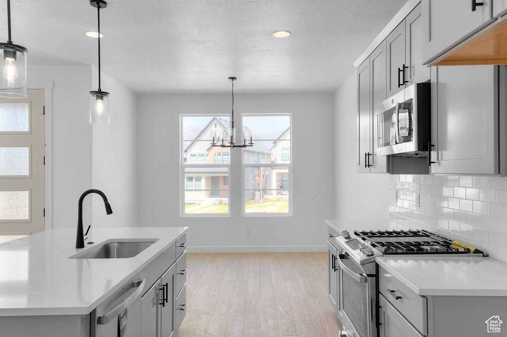 Kitchen featuring stainless steel appliances, a sink, baseboards, light wood-style flooring, and decorative backsplash