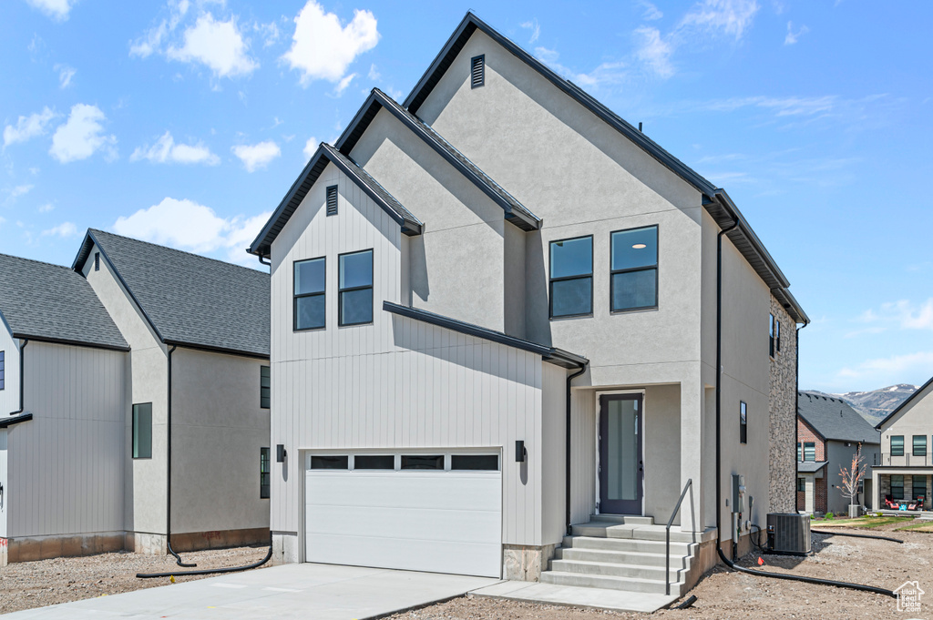 View of front of property featuring driveway, cooling unit, and an attached garage