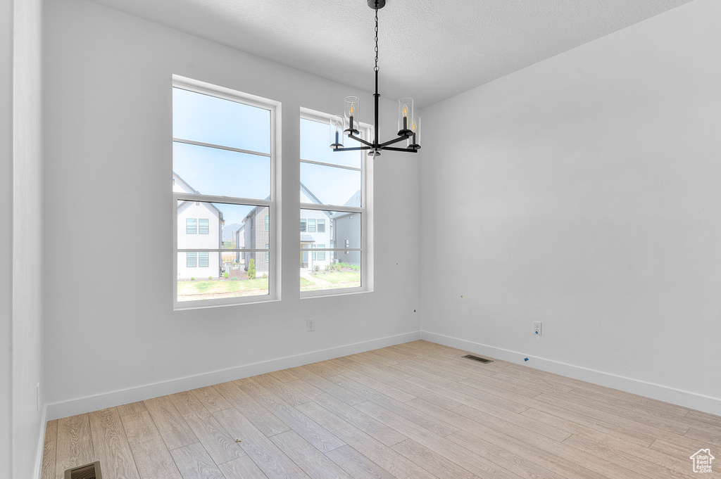 Spare room featuring a chandelier, light wood-type flooring, baseboards, and a textured ceiling