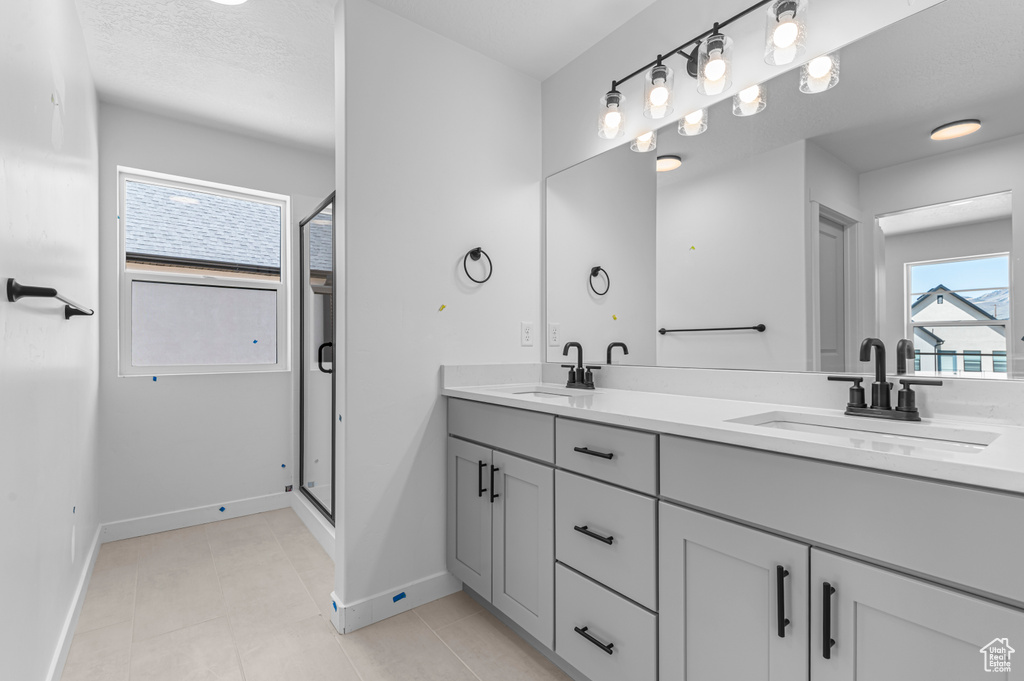 Full bath with double vanity, a shower stall, baseboards, and tile patterned flooring