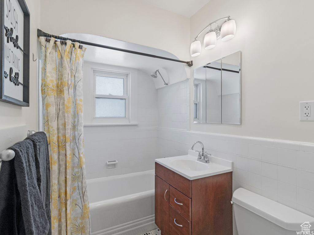 Bathroom with toilet, shower / bath combo, vanity, tile walls, and a wainscoted wall