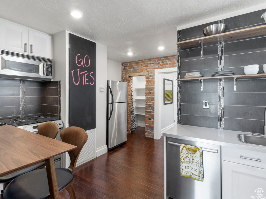 Kitchen with appliances with stainless steel finishes, a sink, dark wood-style floors, white cabinets, and decorative backsplash