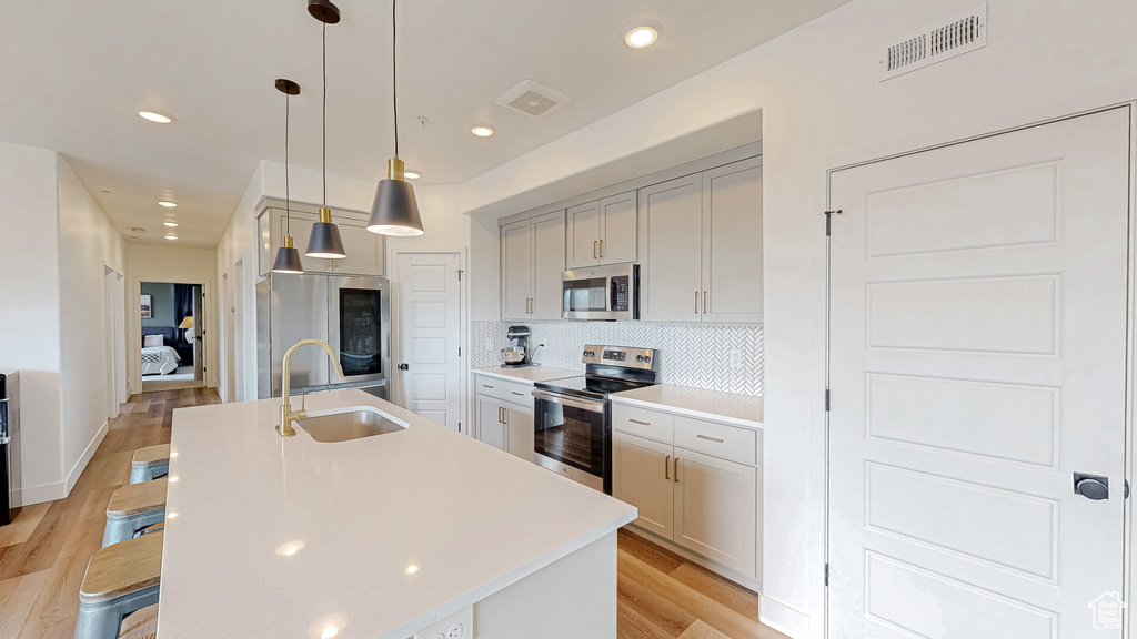 Kitchen featuring appliances with stainless steel finishes, a sink, light wood-type flooring, light countertops, and a kitchen island with sink