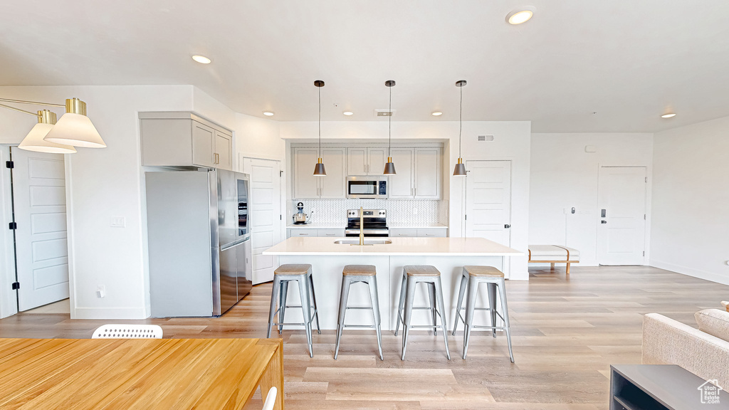 Kitchen featuring appliances with stainless steel finishes, light countertops, decorative backsplash, an island with sink, and recessed lighting